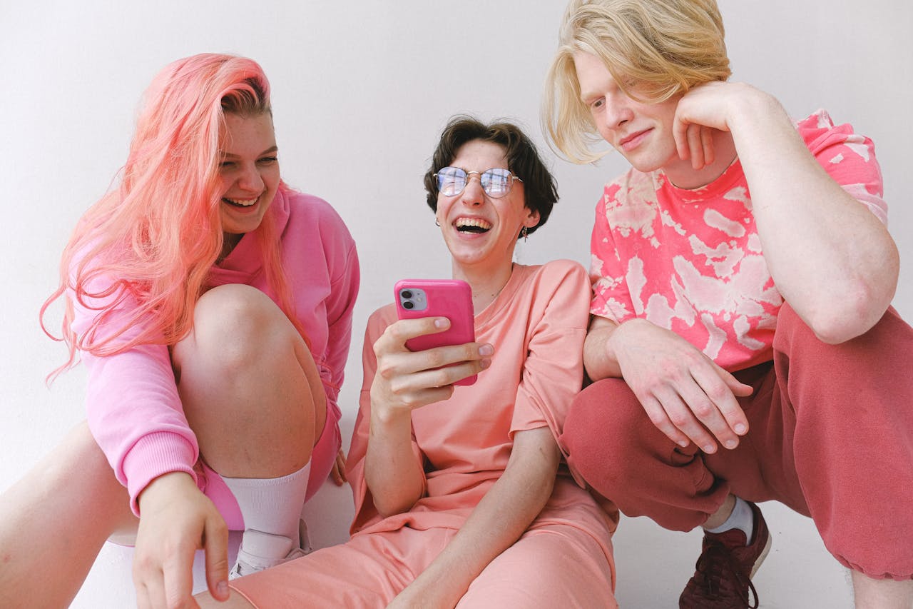 Three friends laughing and enjoying each others company while looking at a smartphone indoors.